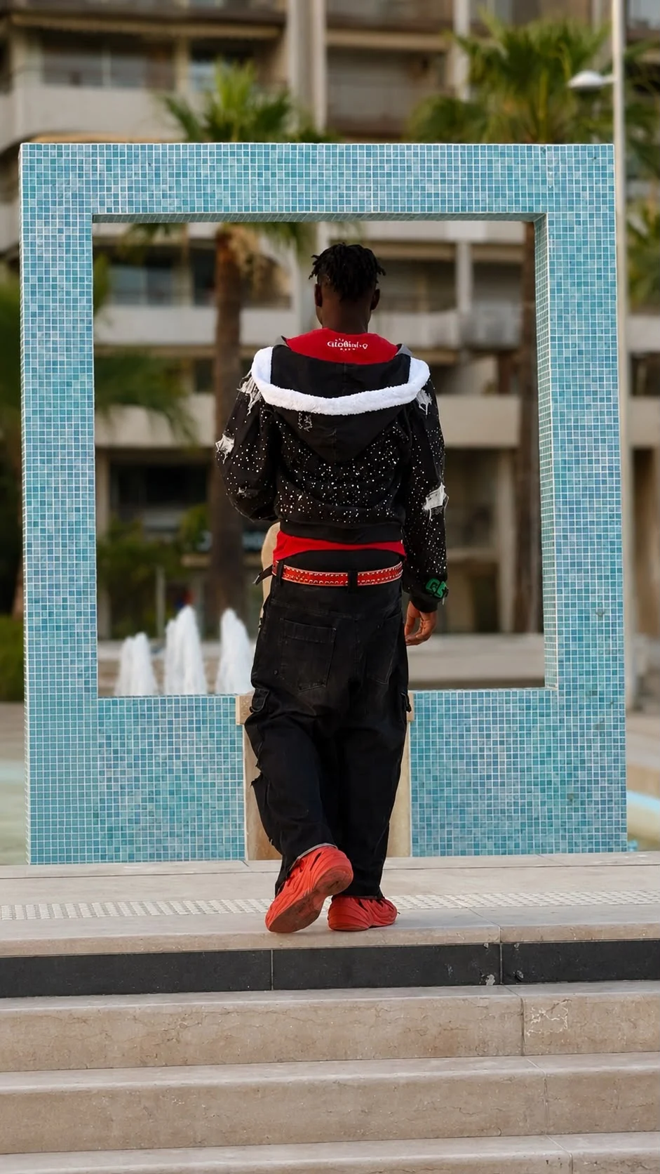 Créateur GBÉ de dos face à la fontaine, veste Héritage